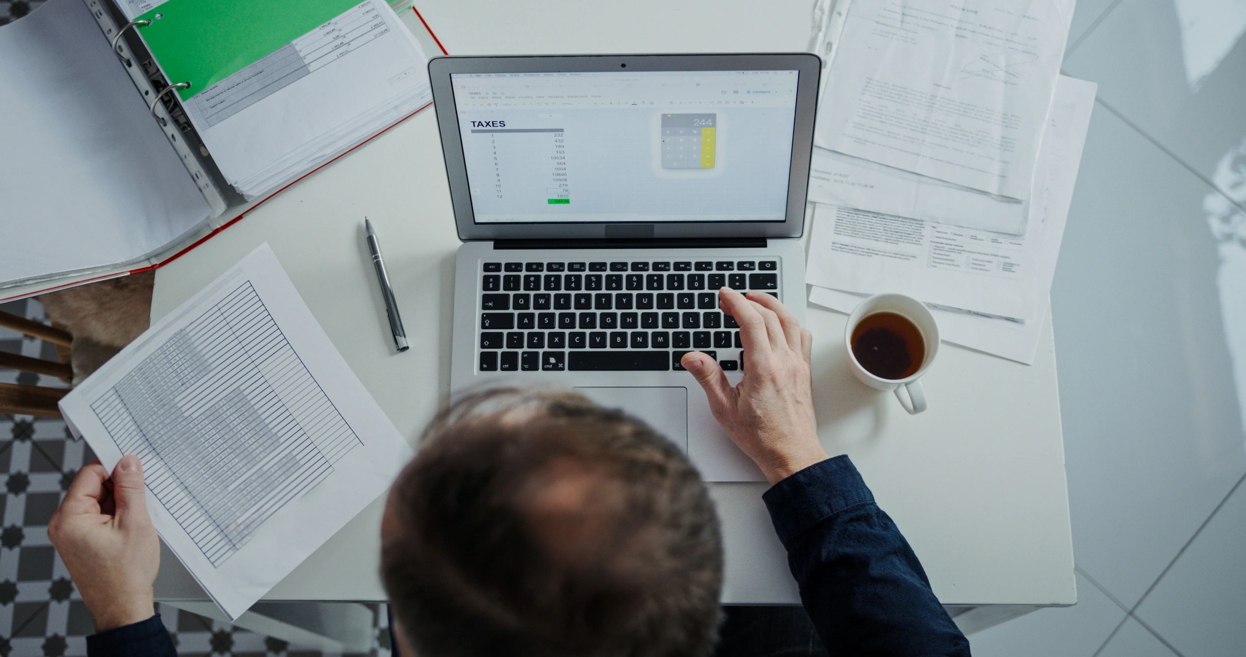 Bookkeeper working on a laptop with financial documents spread across a desk